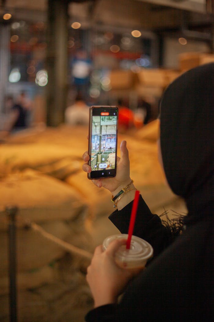 Home A woman using a smartphone while holding a drink inside a coffee shop.